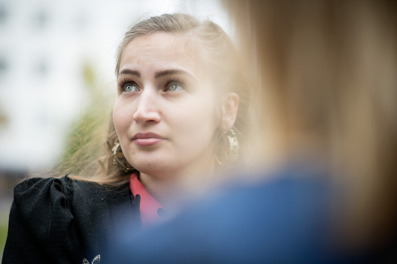Lähikuva nuoresta naisesta, joka katsoo sivulle. Etualalla näkyy epätarkkana toinen henkilö.